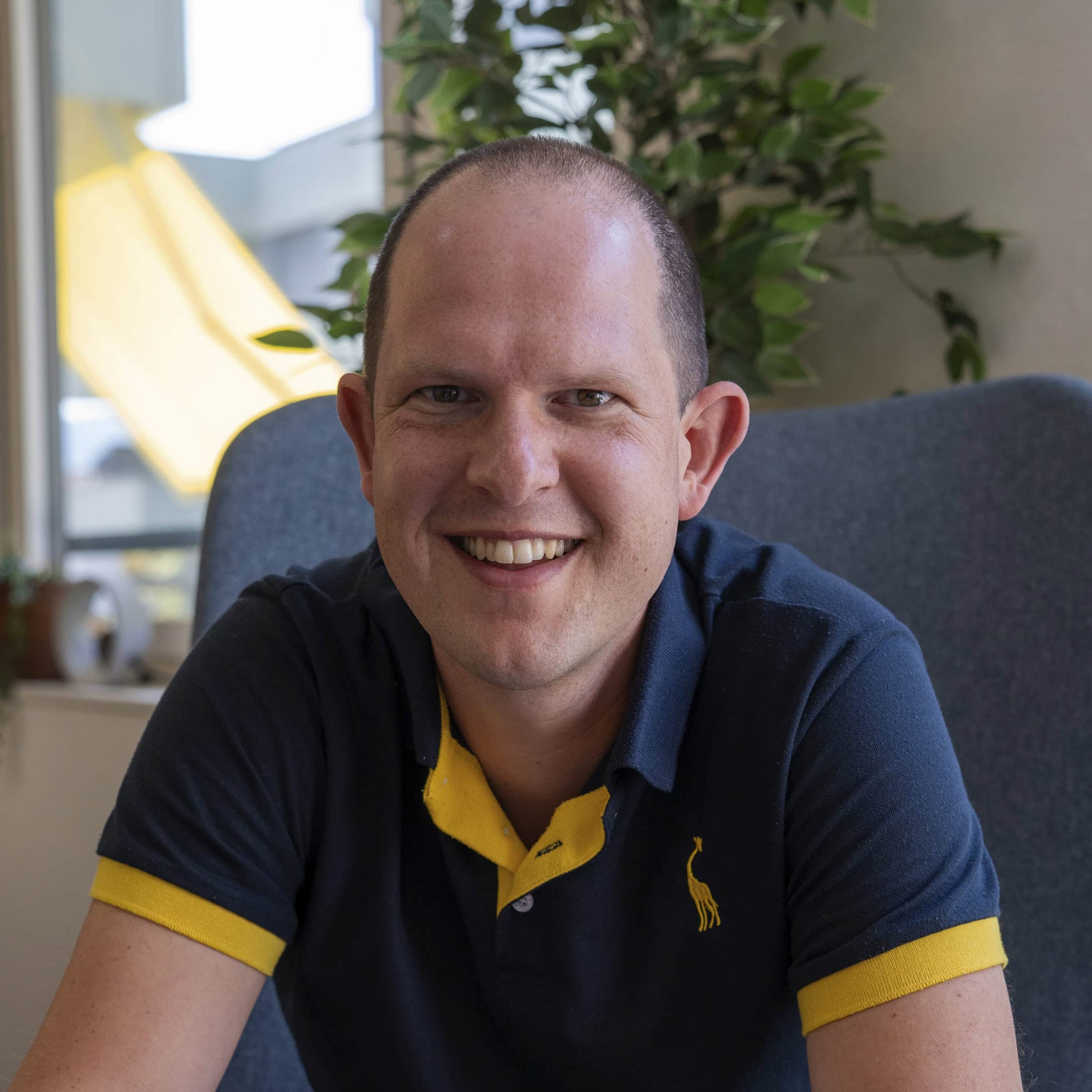 Lächelnder Mann in Poloshirt sitzt auf Stuhl.